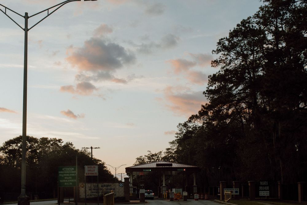 Street lamp illuminates an urban road at dusk with silhouetted trees and pink-tinged clouds in the sky.