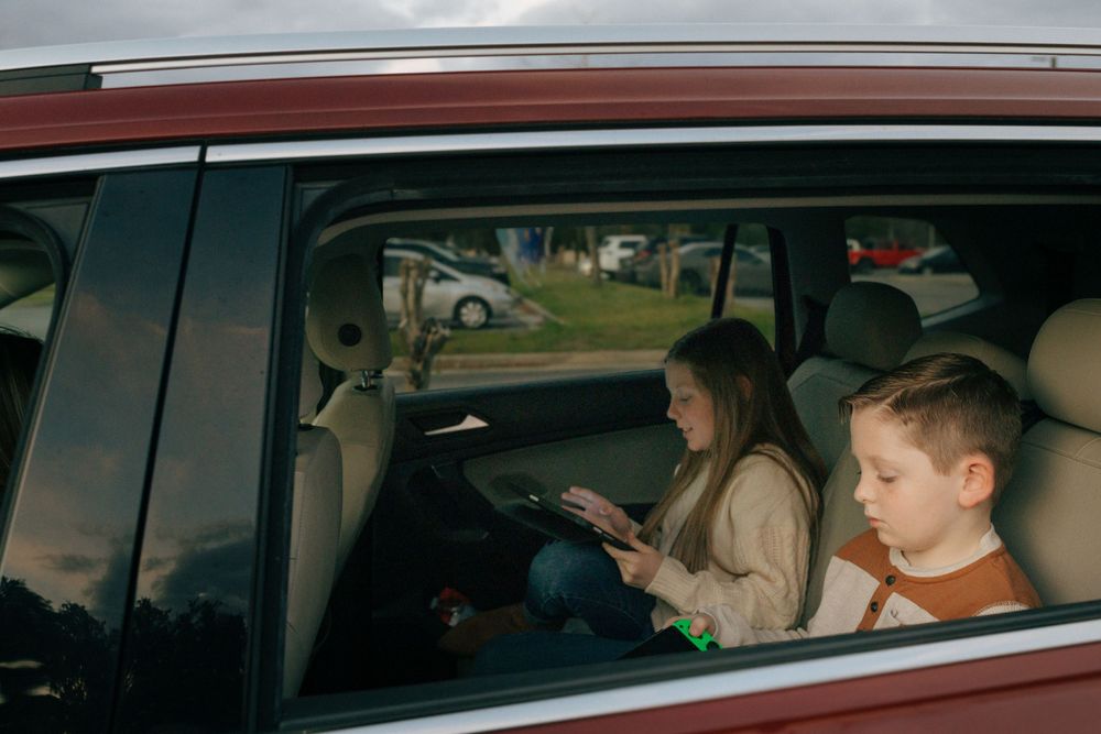 Two passengers in back seat of car look at mobile devices while traveling.