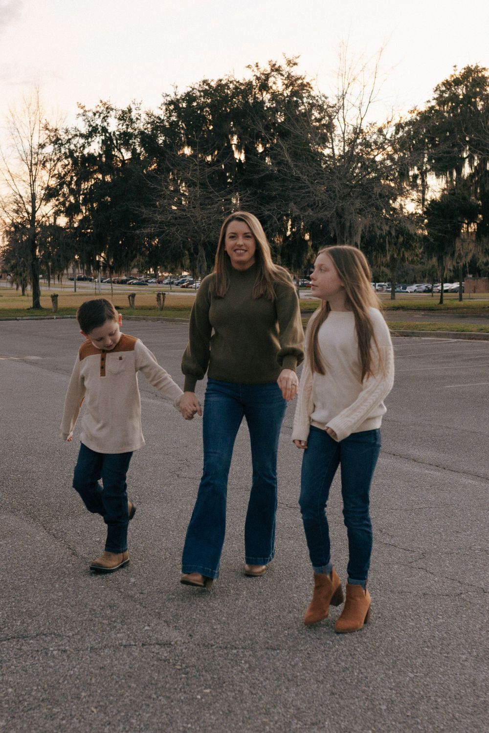 Three people walking together and laughing in a parking lot at sunset with trees in the background.