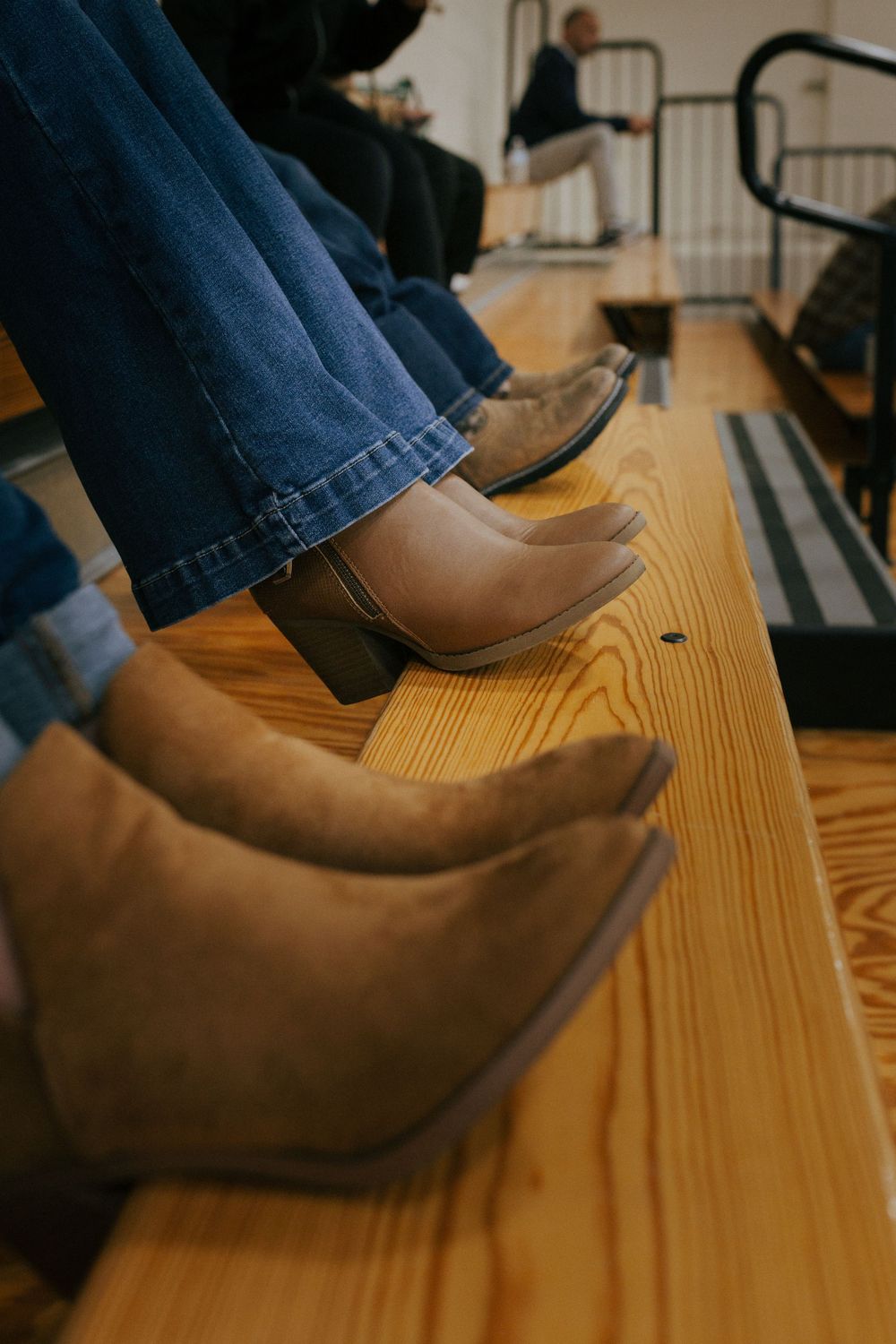 Brown leather boots and blue jeans rest on wooden bleacher-style seating.