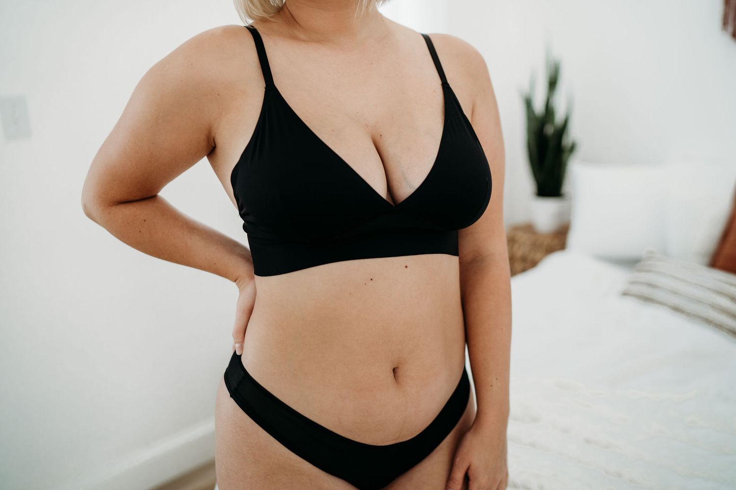 Modern boudoir photography featuring black lingerie set against white wall.