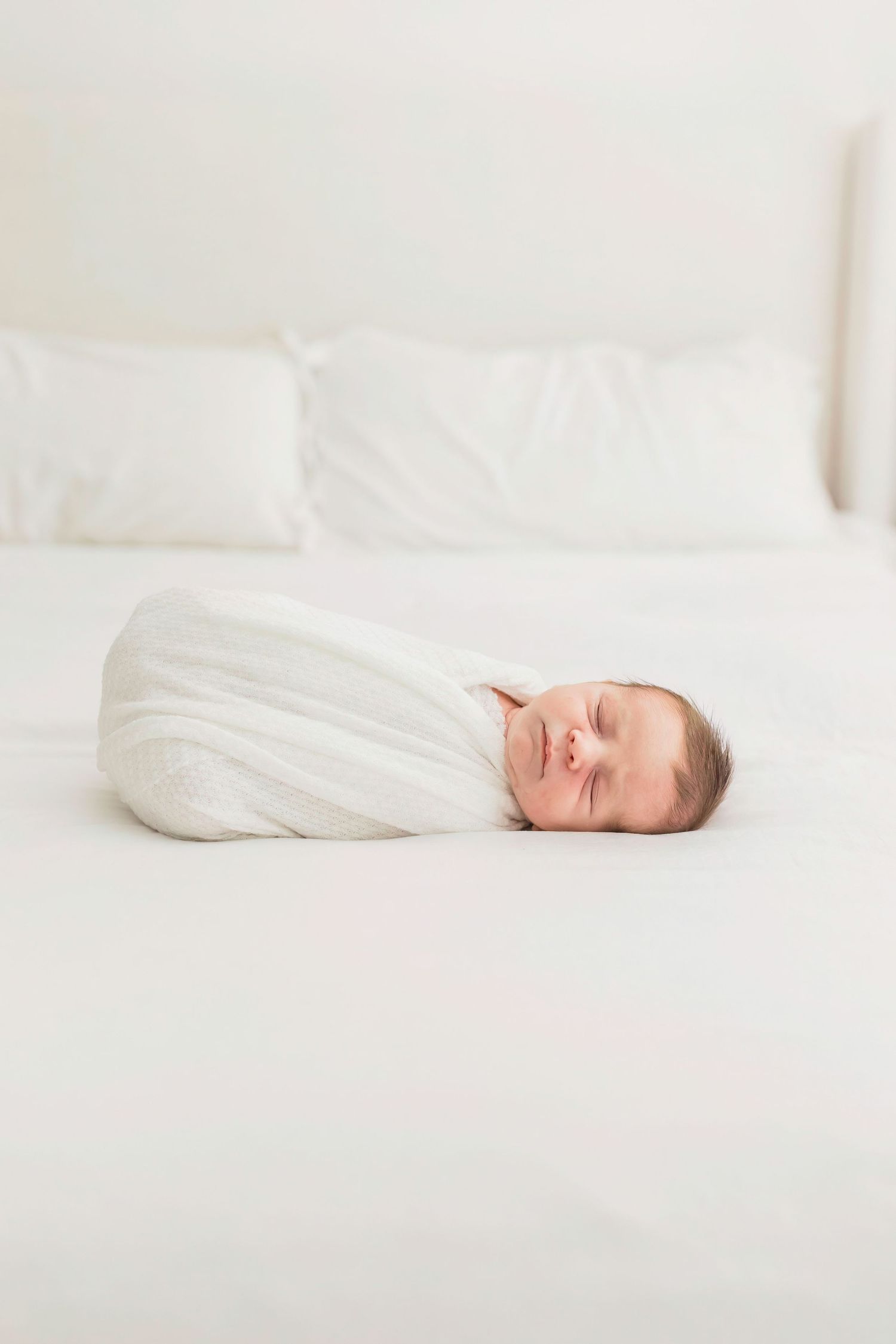 Peaceful newborn sleeping swaddled in white on minimalist bed.