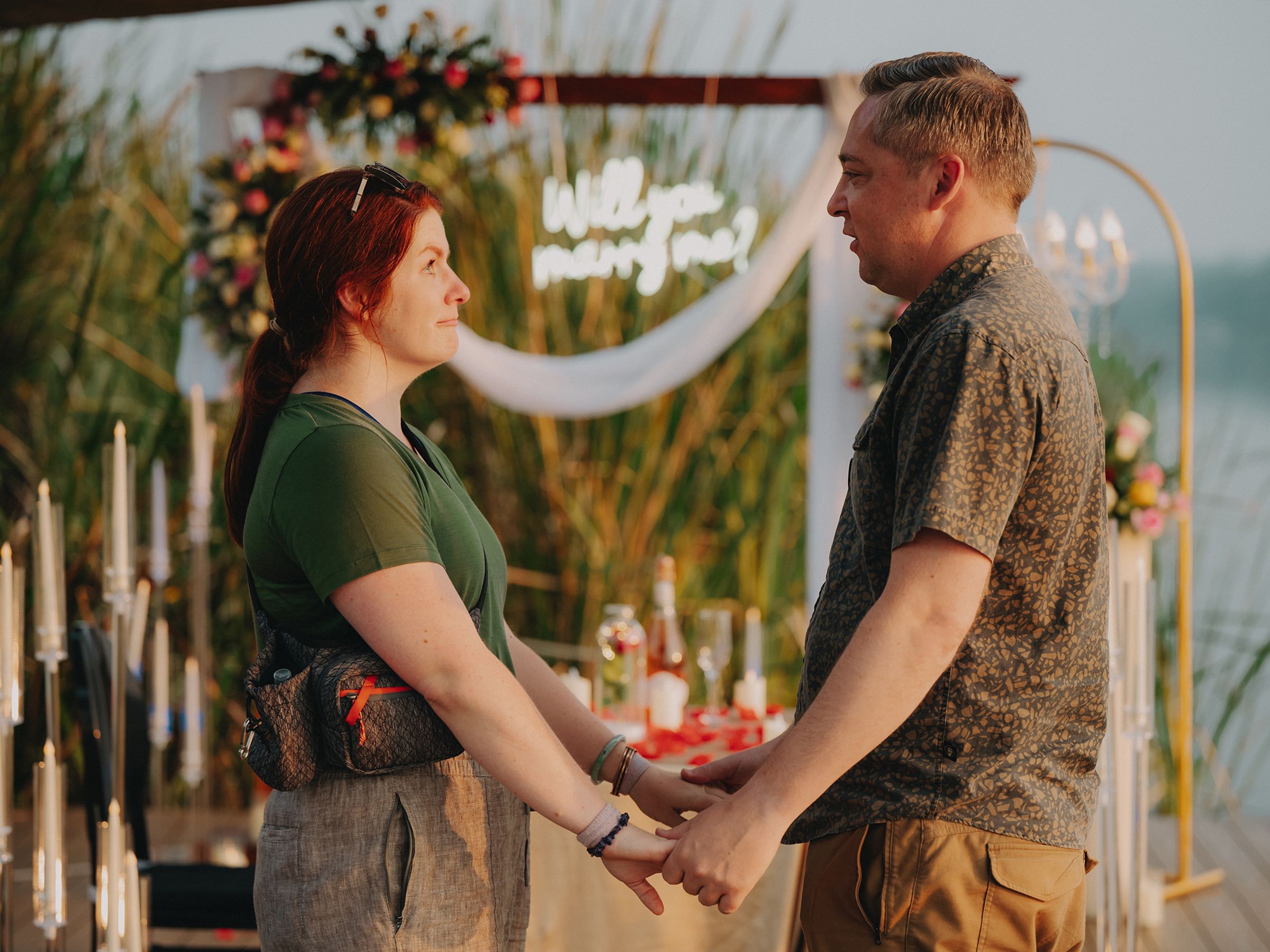 A couple holds hands at an outdoor wedding ceremony with a golden arch and decorative accents in the background.