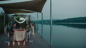 A group gathers for dinner on a wooden dock during dusk overlooking a peaceful lake.