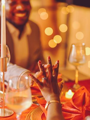 Close up of hands with jewelry against warm candlelit dinner table setting with wine glasses.