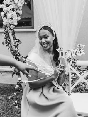 A bride wearing a veil holds a decorative 'BRIDE' sign amid floral decorations.