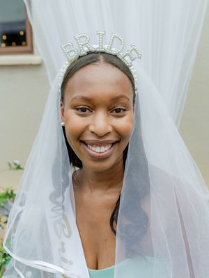 A bride wearing a sparkling 'BRIDE' tiara and veil smiles brightly.
