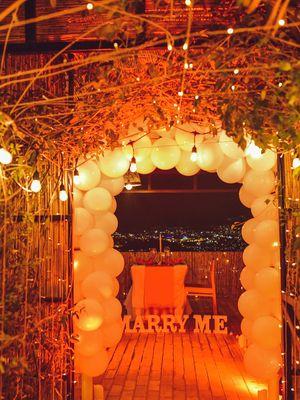 Romantic proposal arch decorated with white balloons and string lights against city backdrop.