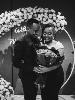 Marriage proposal moment under a white floral arch with illuminated signage.