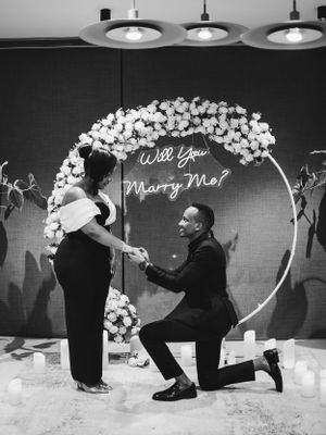 Marriage proposal scene under floral arch with pendant lights overhead.