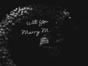 Illuminated proposal sign with white floral arch in dark romantic setting.