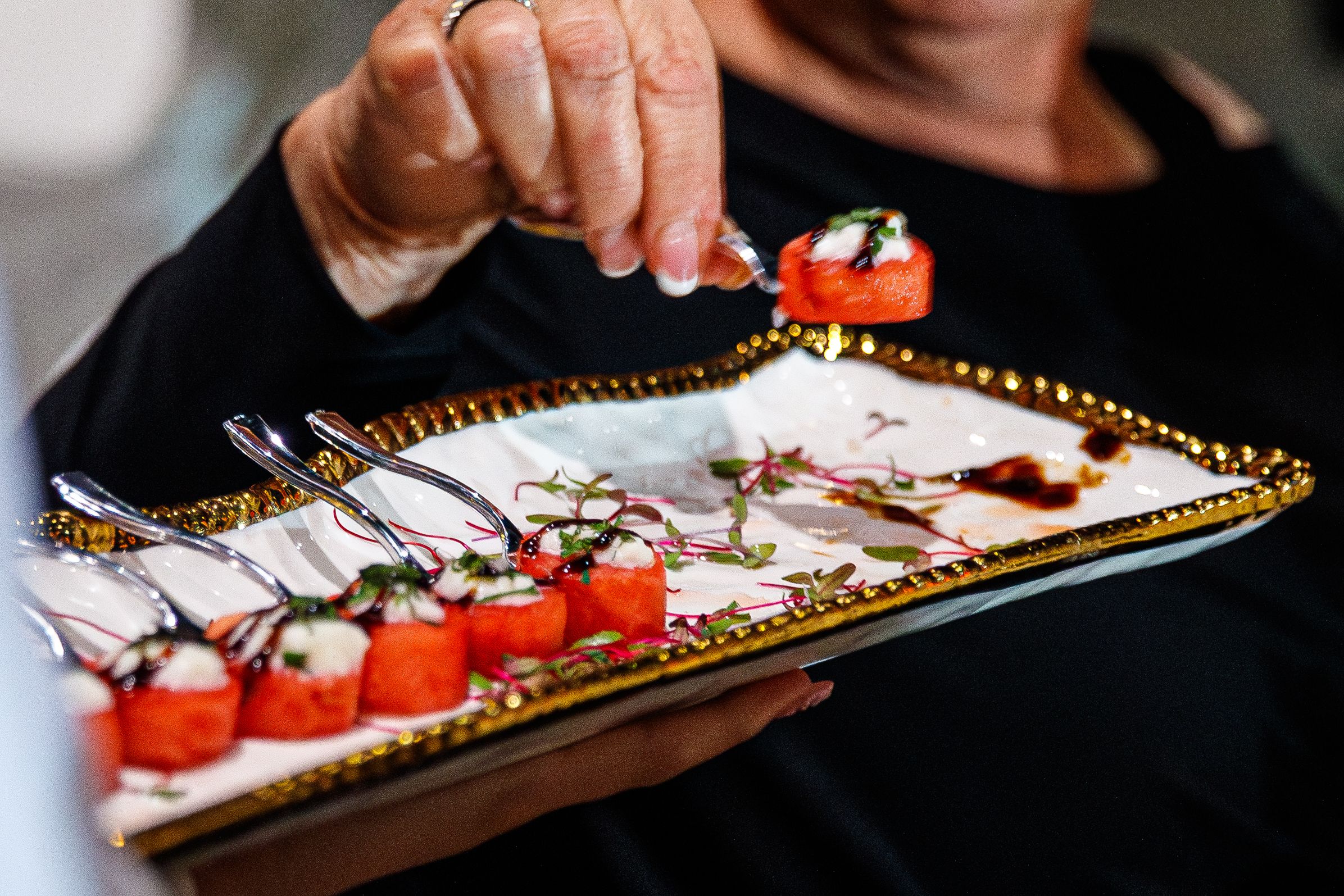 Someone holding an elegant gold mirrored tray with cherry tomatoes and appetizers being served at an event.