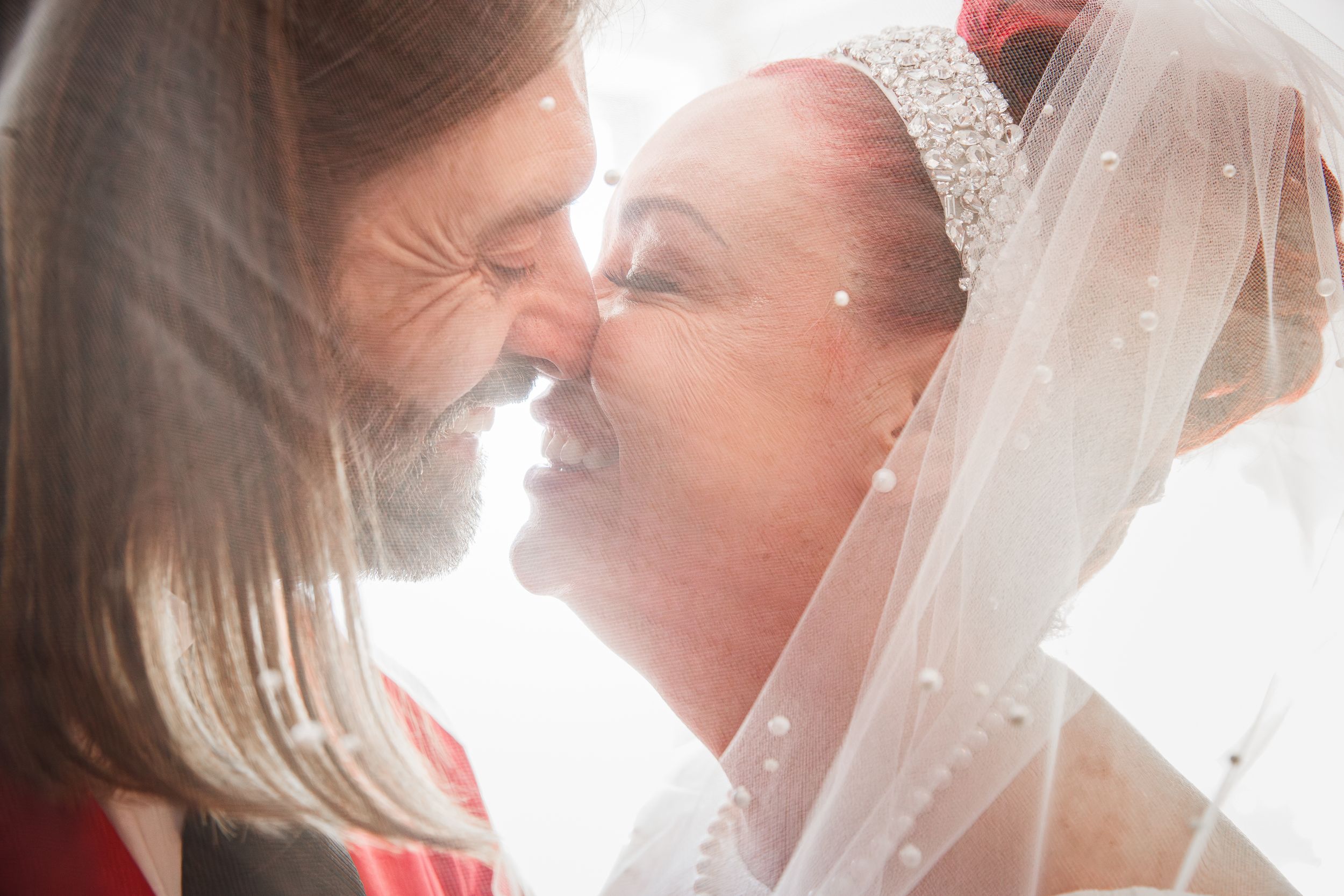 A couple shares a tender romantic moment during a wedding ceremony while wearing white and red attire.