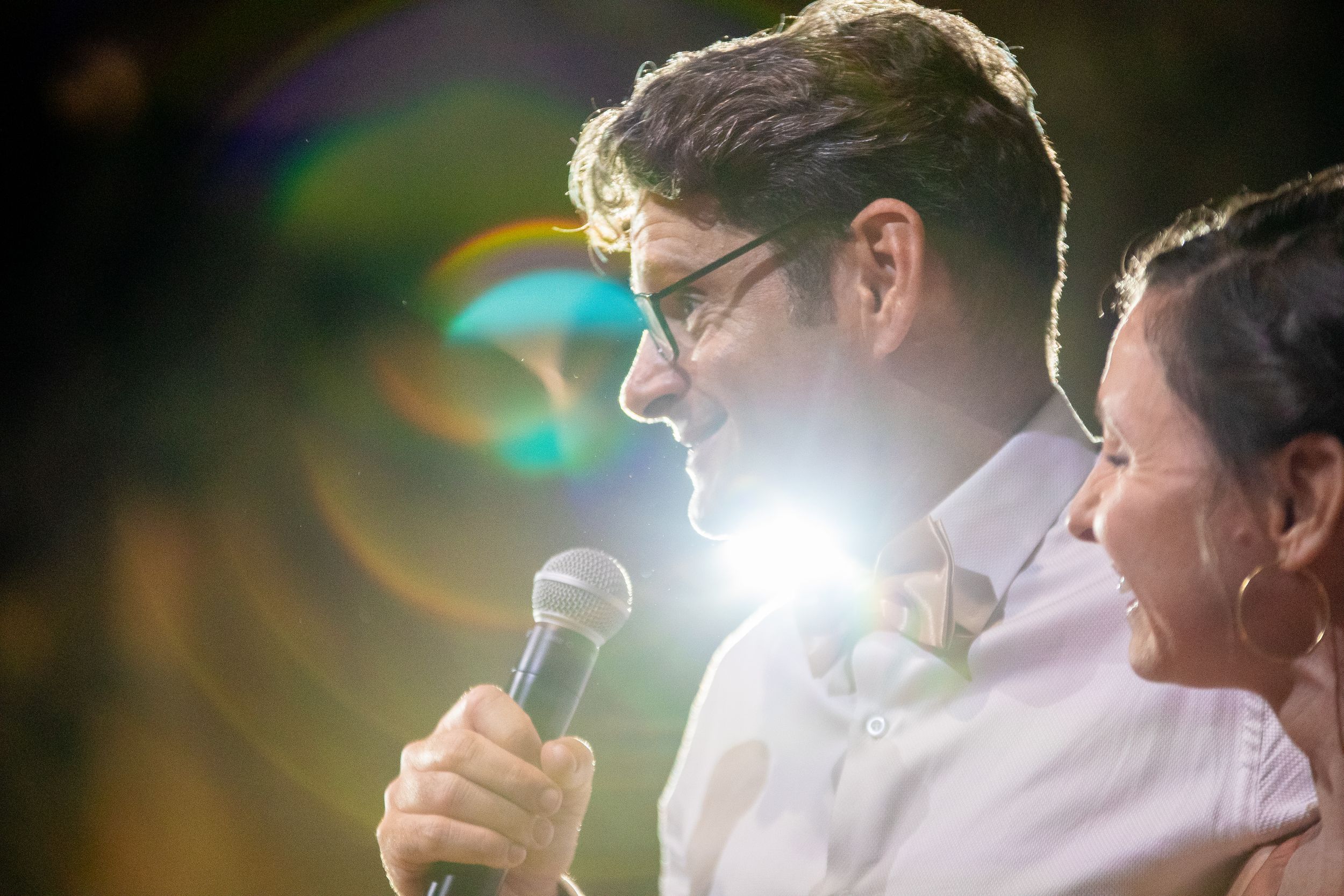 A sequence of overlapping images shows people speaking into microphones with lens flares and bright lighting effects.