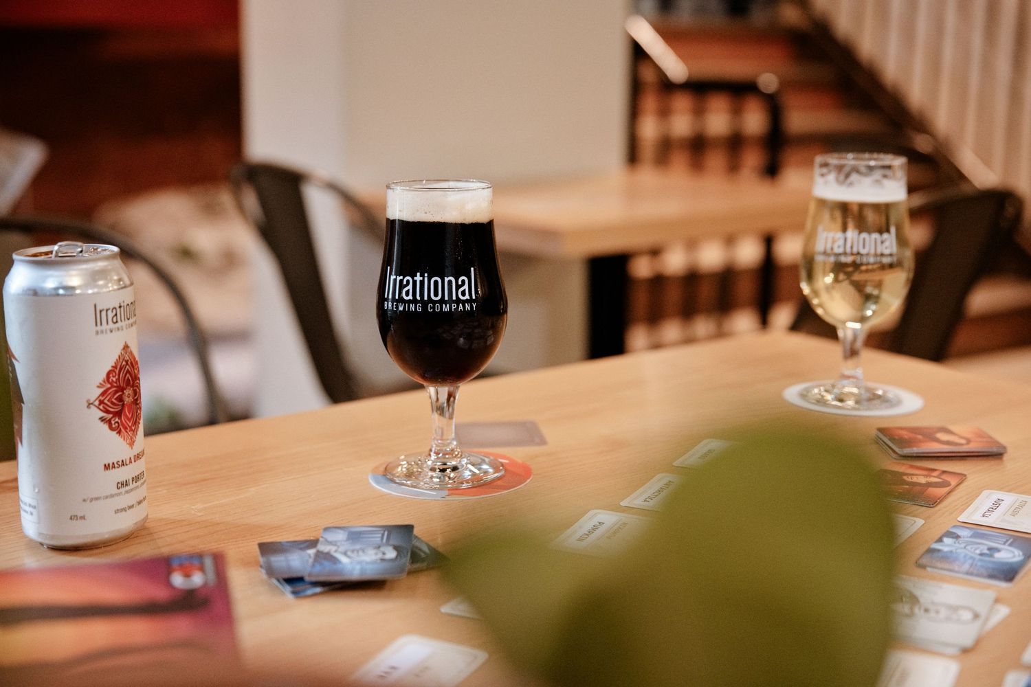 Irrational Brewing Co. craft beer glasses and cans displayed on a wooden table in a cozy taproom setting.