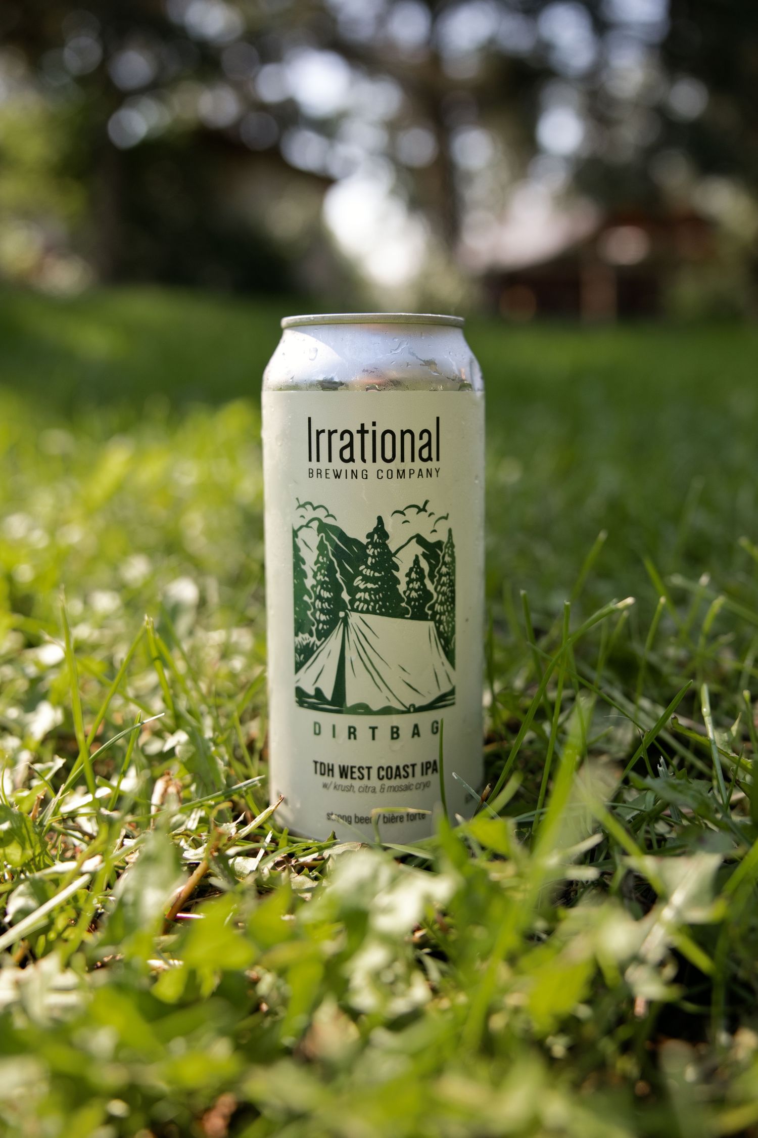Irrational Brewing Company Dirtbag West Coast IPA beer can sitting in green grass outdoors in natural sunlight.