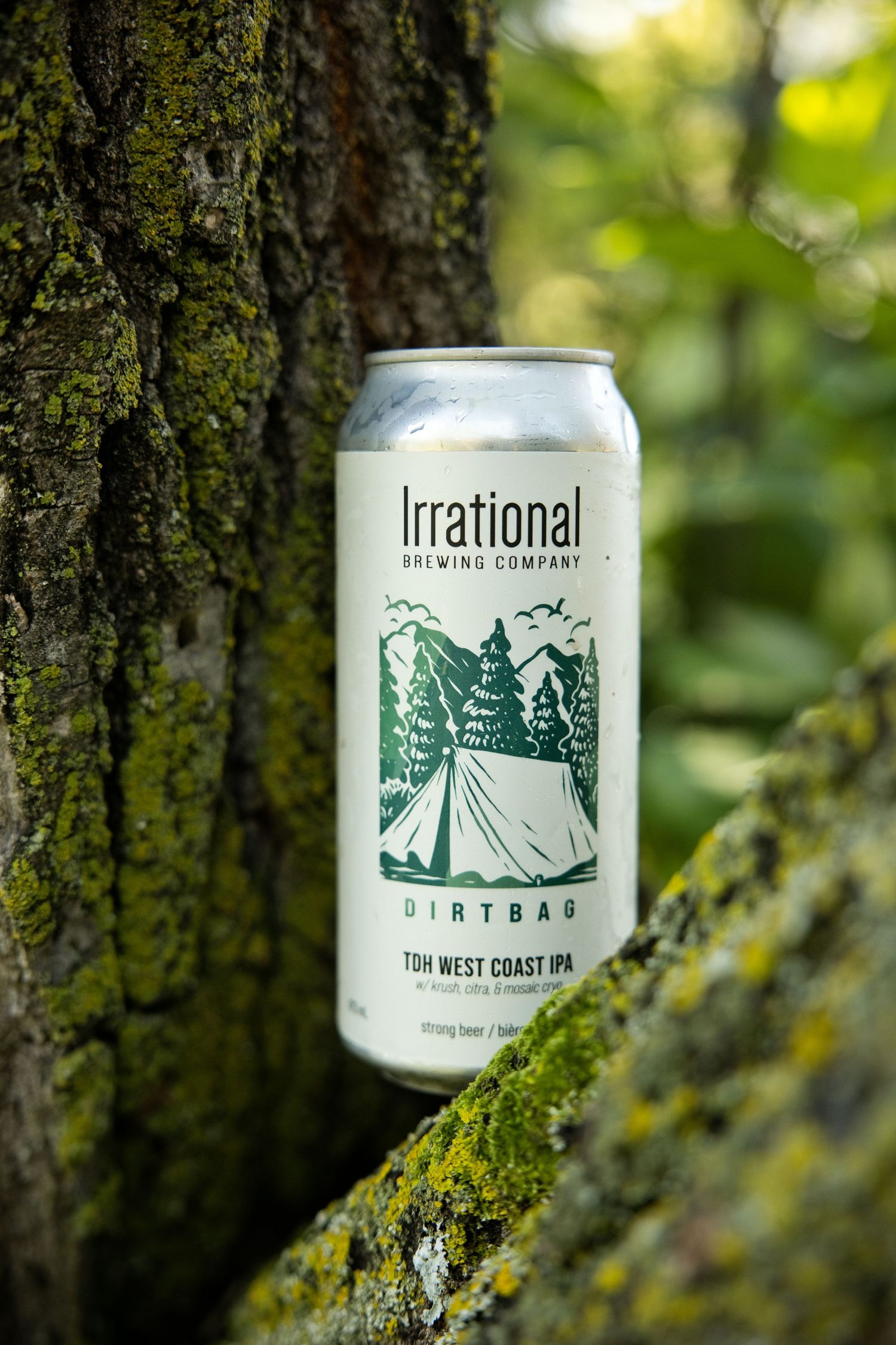 Irrational Brewing Company Dirtbag West Coast IPA beer can resting against a mossy tree trunk outdoors.