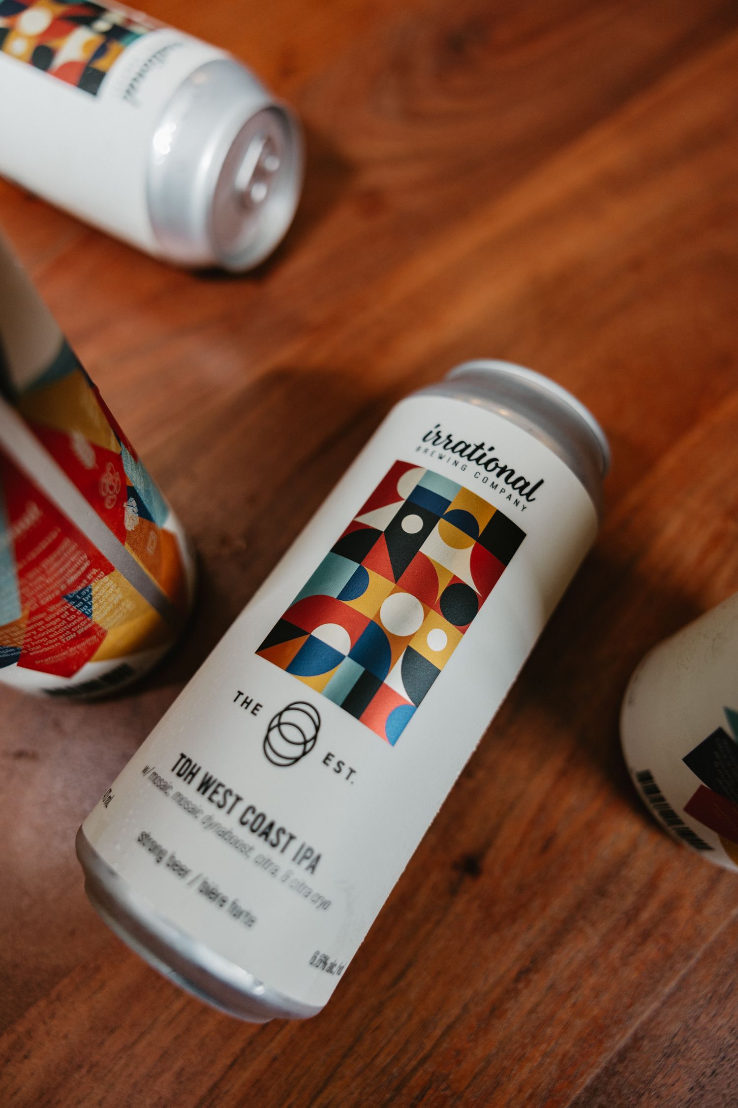 Irrational Brewing TDH West Coast IPA craft beer can on a wooden table with colorful geometric label design.