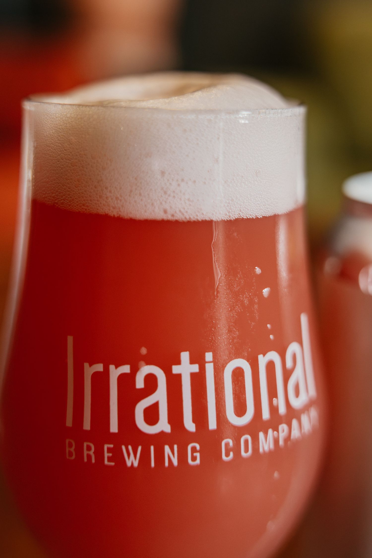 A glass of red craft beer with white foam head, branded with Irrational Brewing Company logo.