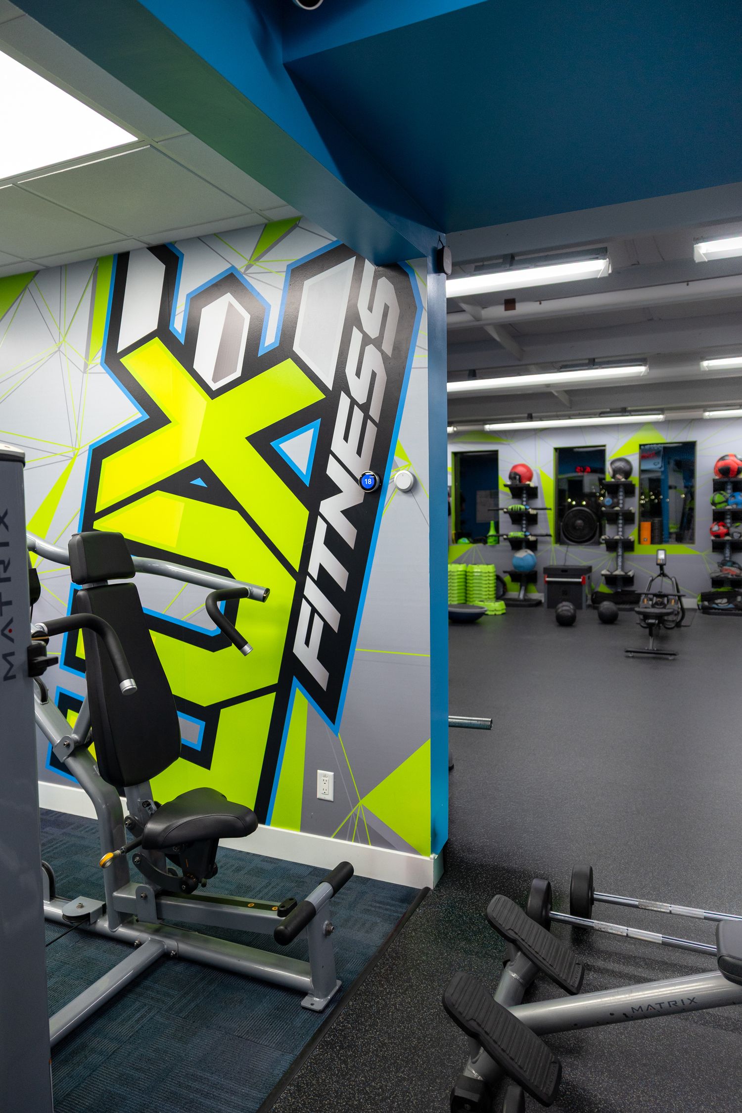 EXF Fitness gym interior with colorful wall mural, weight equipment, and exercise accessories on display racks.