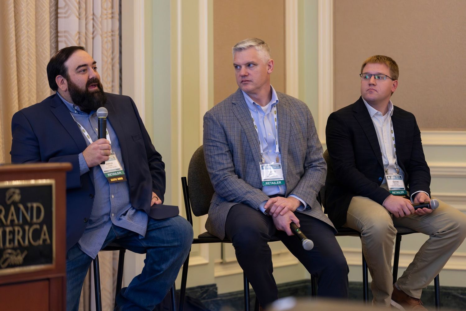 Business professionals seated in a row at a conference panel discussion in an elegant room with yellow walls.