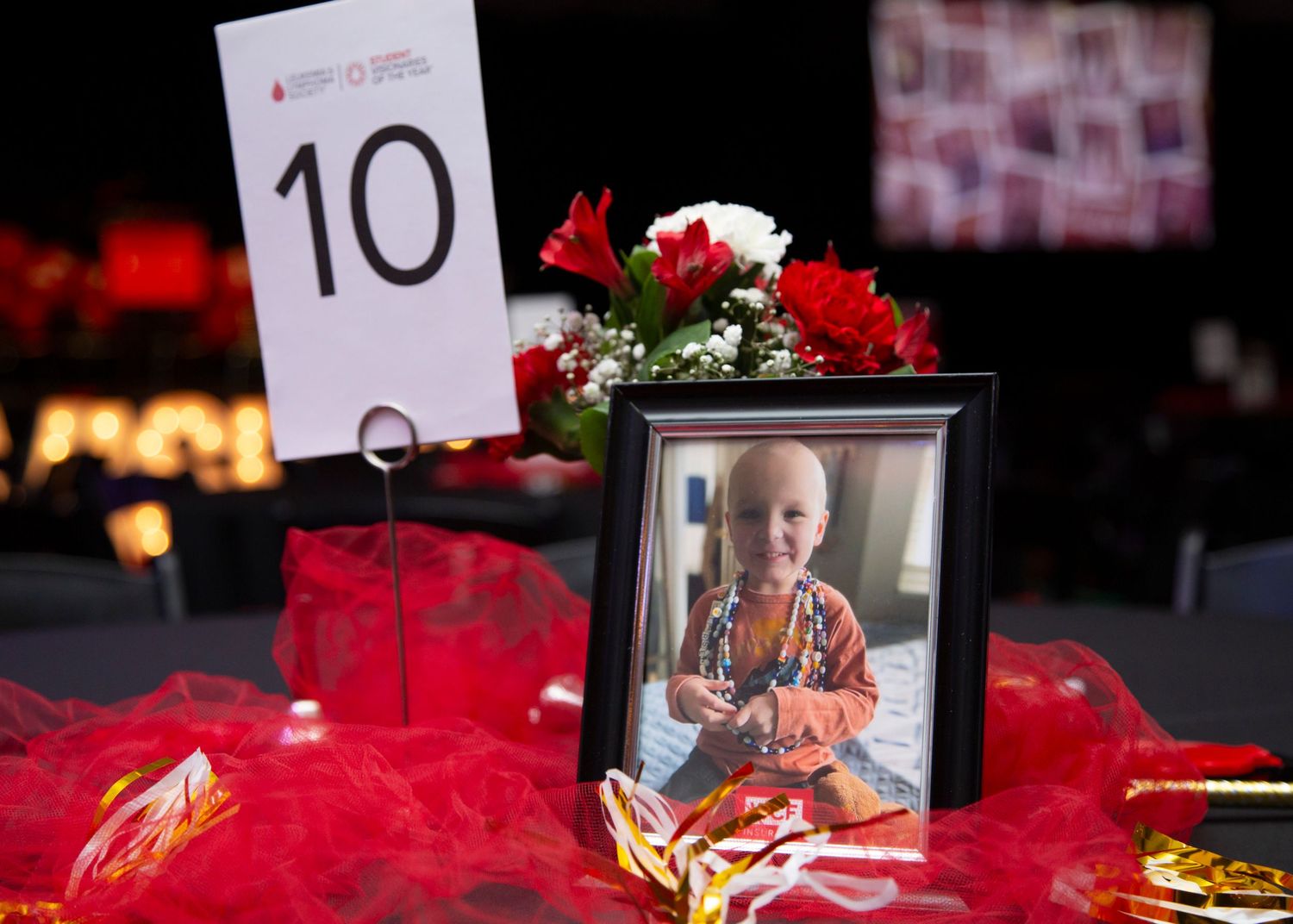 Memorial site with multiple framed photographs and red floral arrangements on a dark table display.
