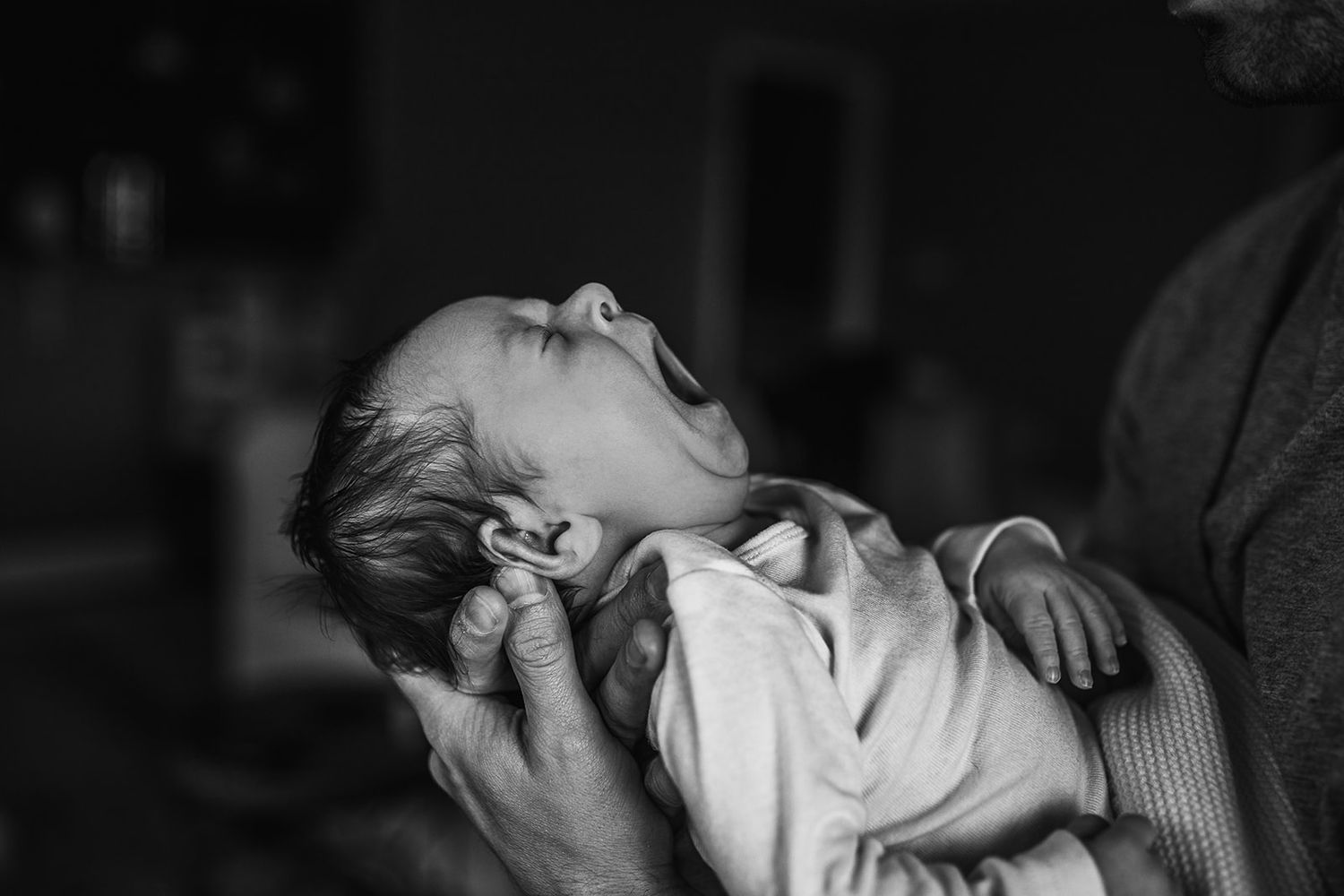 A father holds his son while the newborn shows off his yawn.
