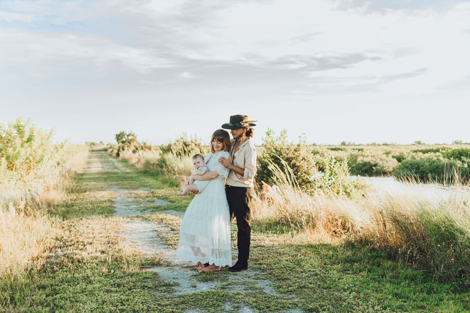 A romantic embrace between newlyweds in a sunlit field with natural landscaping.