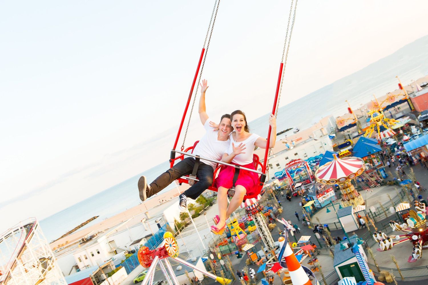 Couple enjoying swing ride at carnival with colorful amusement park scenery in background at sunset.
