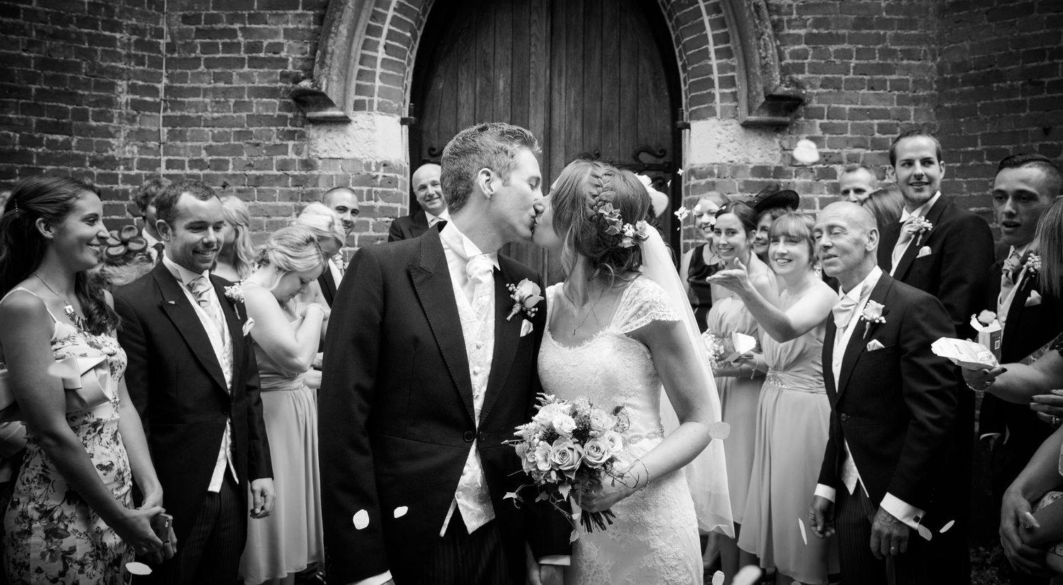 Black and white panoramic shots of wedding guests celebrating outside a brick building.