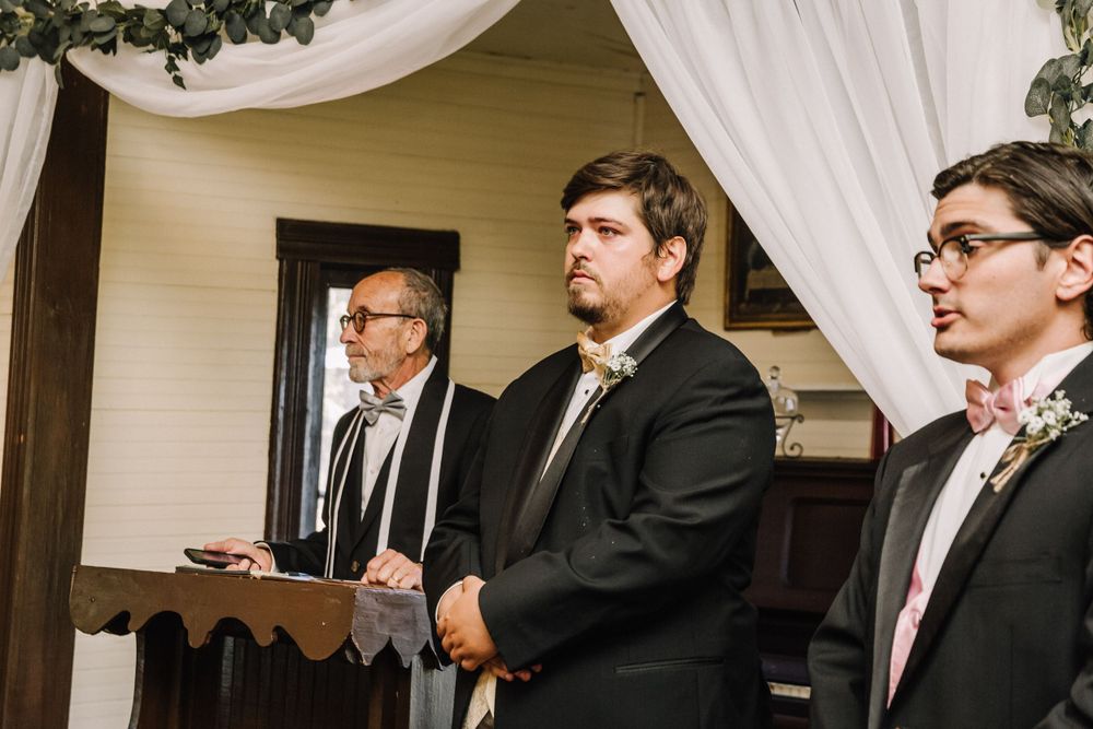 Three formally dressed attendants standing at attention during an indoor ceremony.