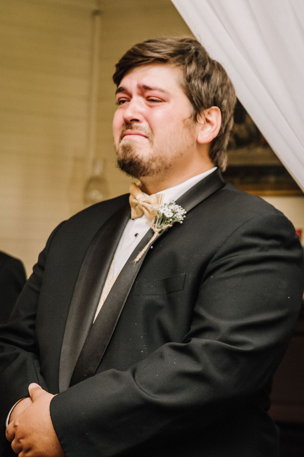A formal portrait of an attendant in a black tuxedo with a boutonniere.