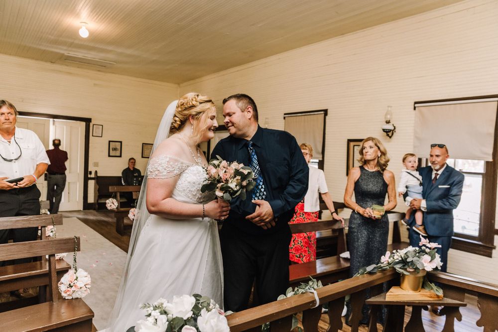 Intimate wedding moment during indoor ceremony with wooden pew seating.