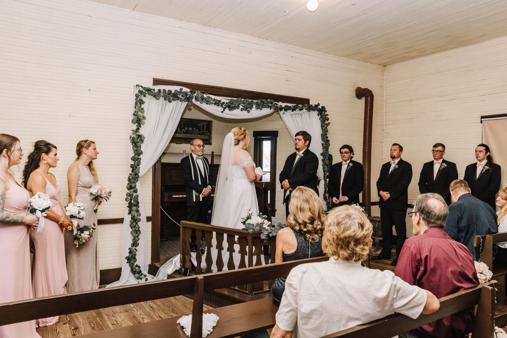 Wedding ceremony in historic chapel with bridal party and guests watching from wooden pews.