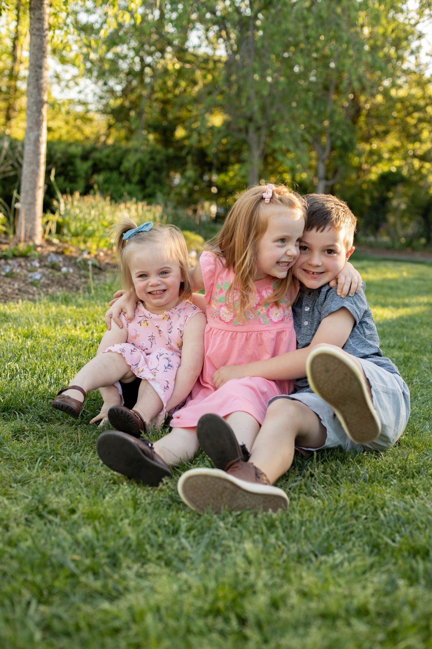 Young children sitting together on grass sharing laughs during an outdoor photoshoot.