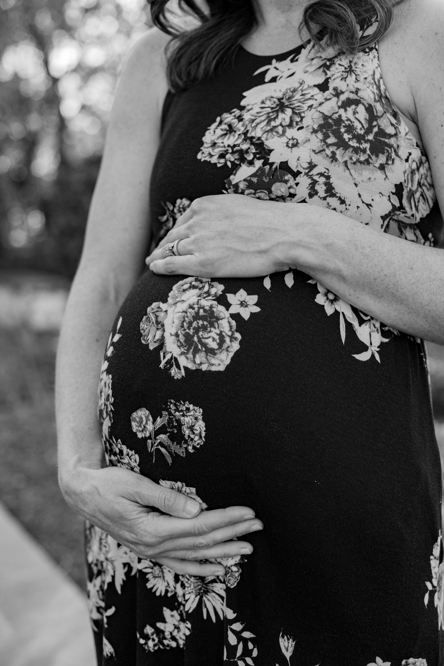 Black and white close-up shots of hands cradling a pregnant belly in a floral dress.