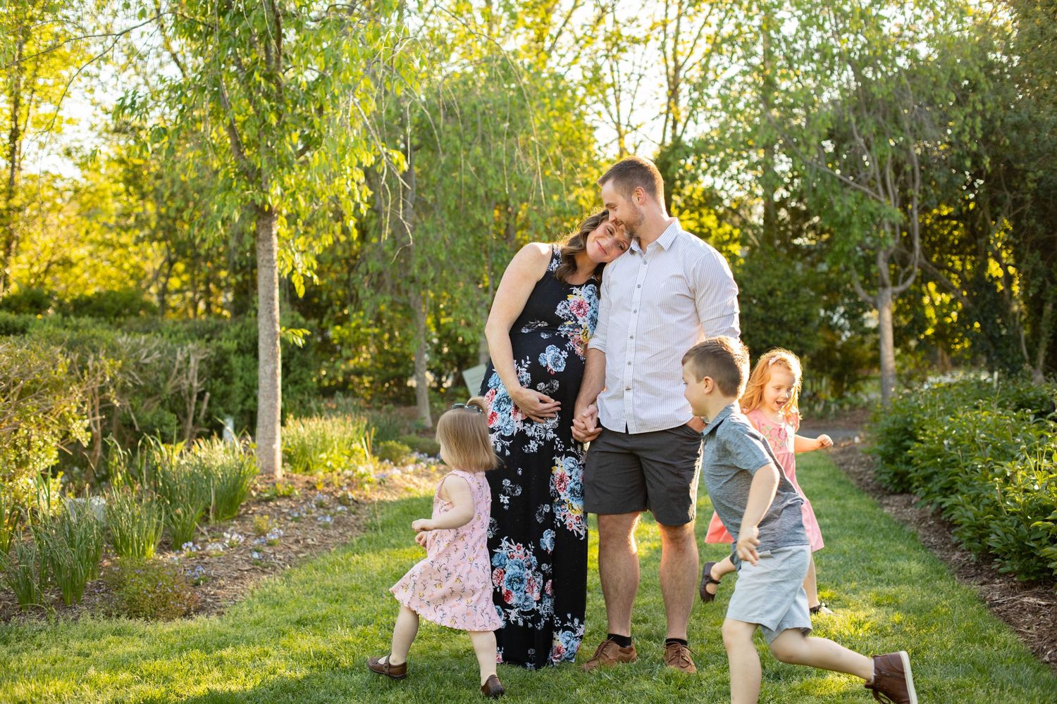 Family portrait session in a sunlit garden path with blooming flowers.