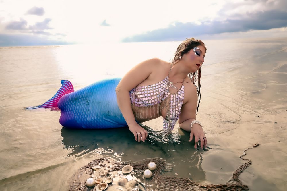 Person in mermaid costume playing in shallow ocean waters at sunset.