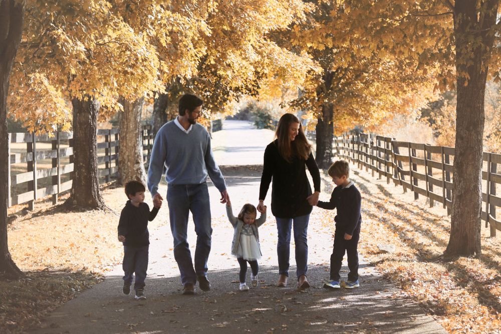 Family walks together on wooden bridge path surrounded by autumn trees with golden leaves.