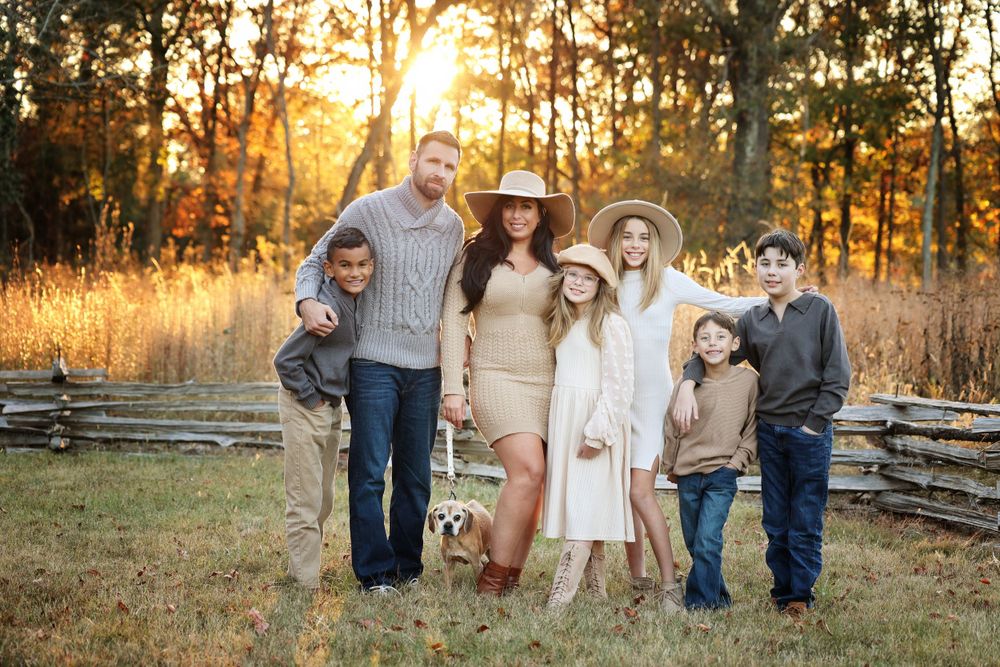 Family in coordinating neutral outfits poses together in autumn field at sunset during Fall Family photo session.