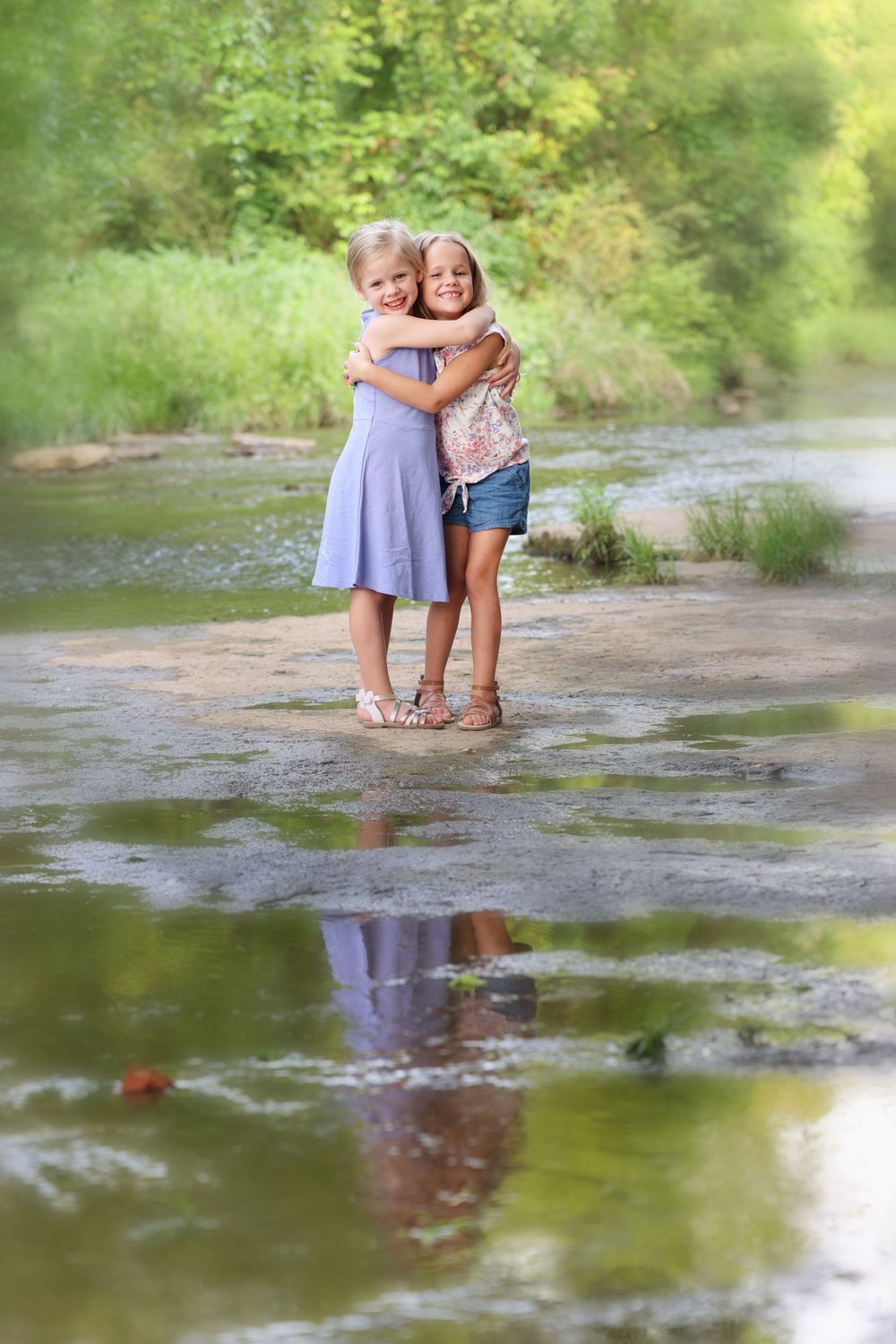 Two children hugging each other while standing in a shallow stream in photo session in Nolensville TN.