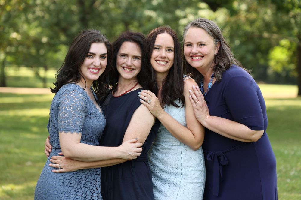 Four women wearing casual dresses pose together outdoors in a park setting in Large Family Session Nashville TN.