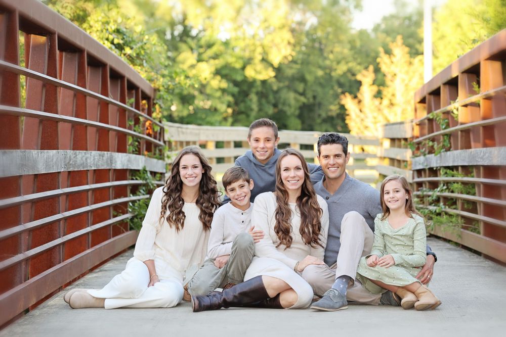 Family sitting together on wooden bridge during outdoor portrait session in casual white clothing DT Nolensville, TN