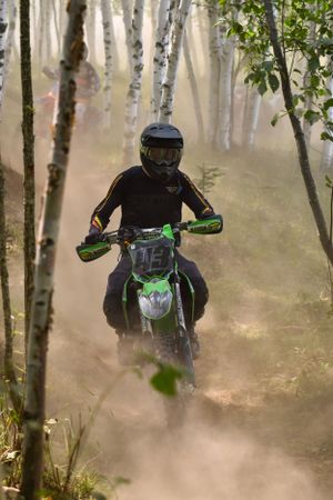 Dirt bike rider navigates through misty birch forest on an off-road trail.