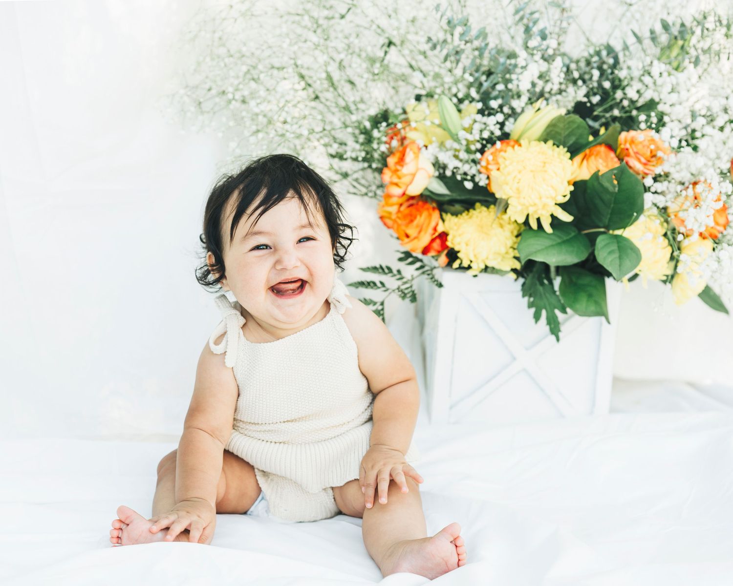 Bright and airy baby portrait session with yellow and orange floral arrangements.