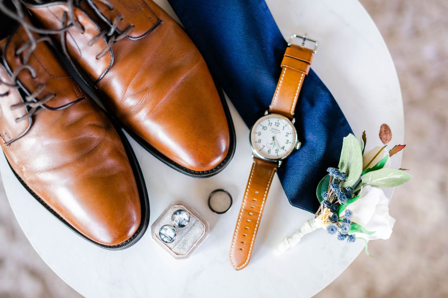 A collection of men's wedding accessories including shoes, a watch, and a boutonniere.
