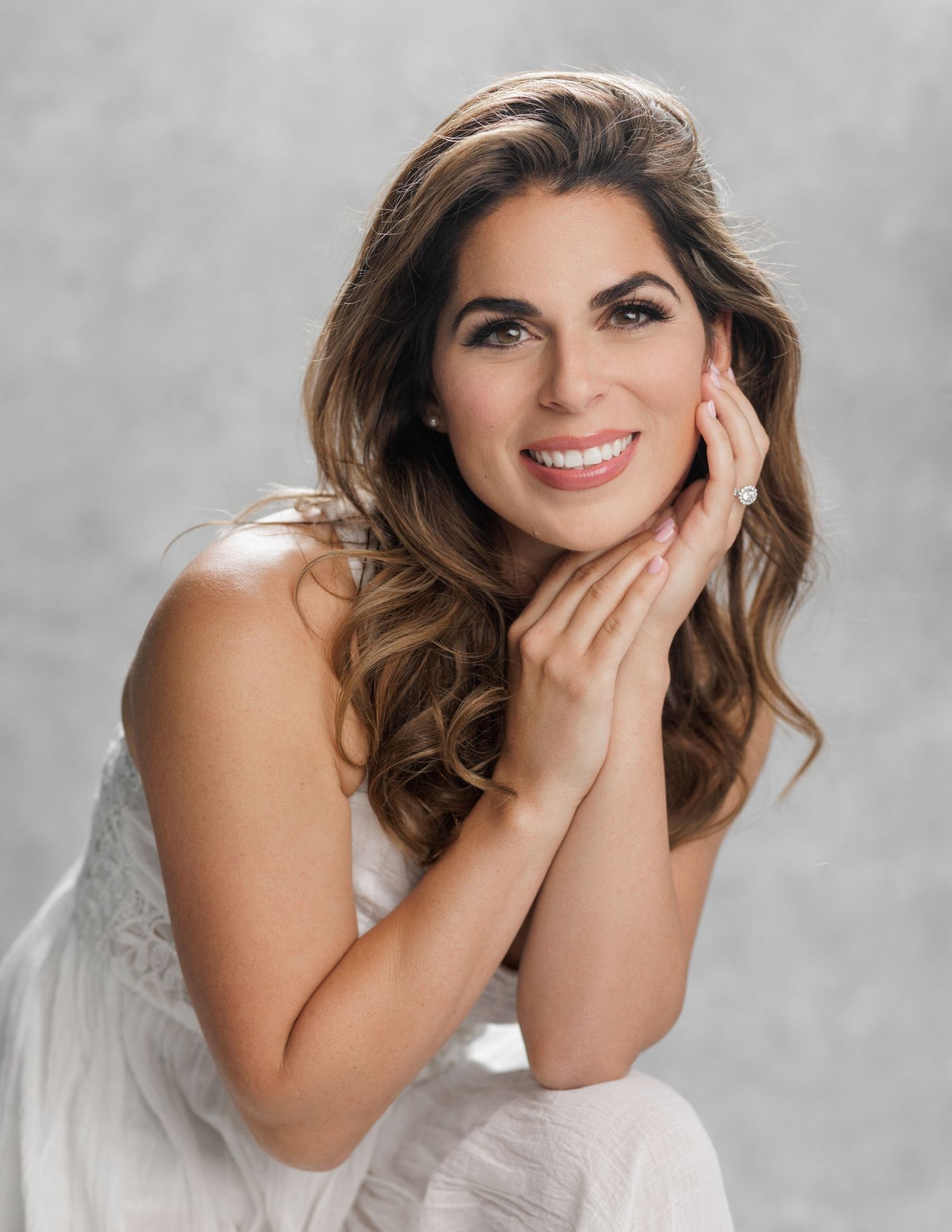 Studio portrait in soft lighting featuring white lace dress and elegant styling.