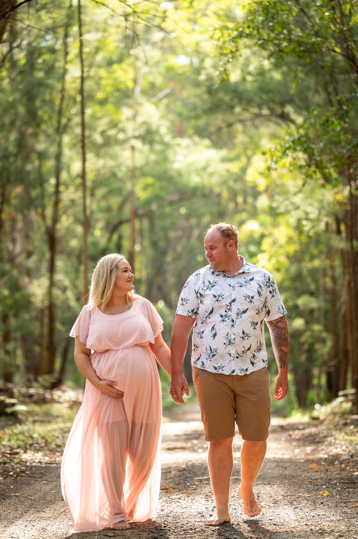 expecting parents walking together looking at each other lovingly in the bush