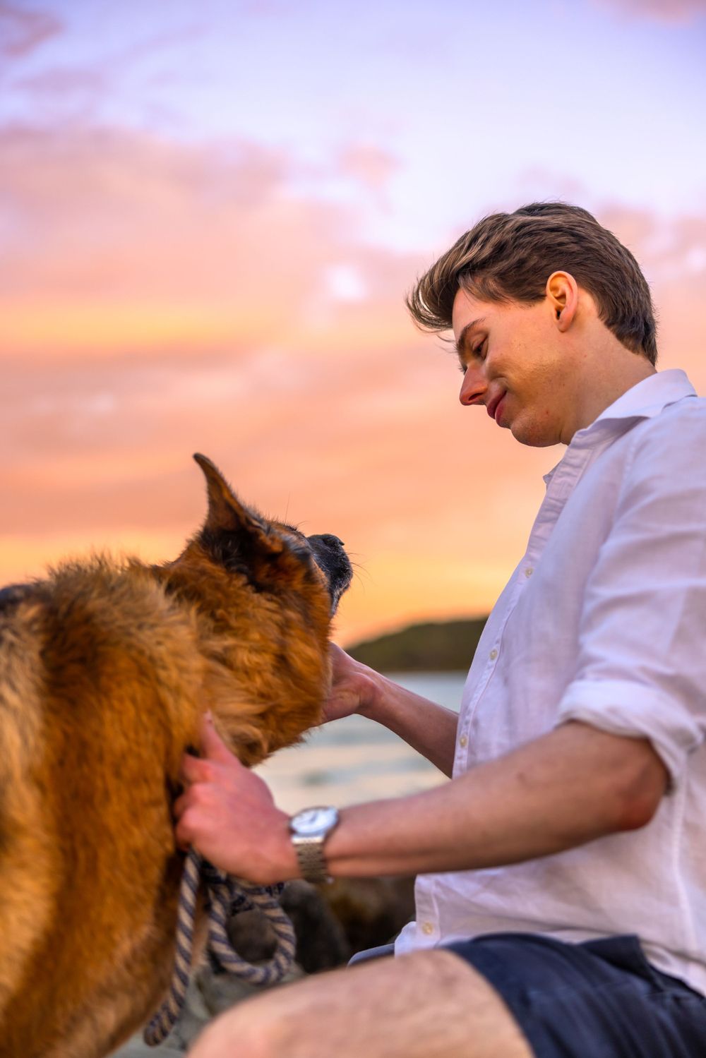 A man and his dog sitting on the rocks at Noosa staring at each other while the sun sets away