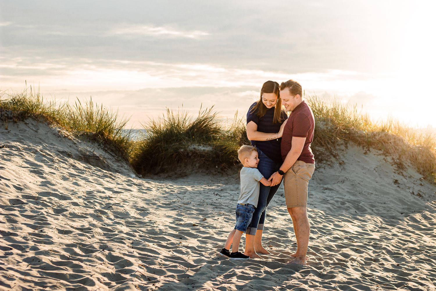 On a beach on Hayling Island a family of three stand close together hugging in the sunlight.